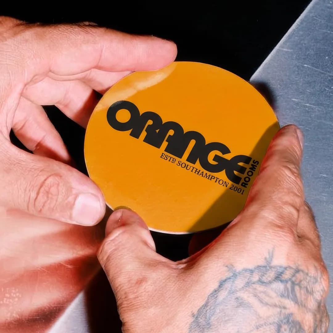 Orange Rooms branded coaster held in a hand